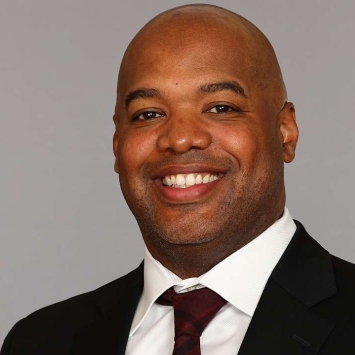a Black man wearing a suit and tie on a grey background