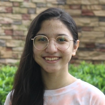 a young woman with glasses and dark hair wearing a tie dye shirt