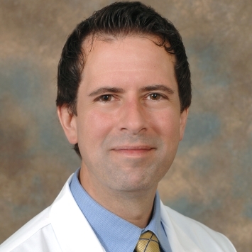a young man with dark hair wearing a doctor's coat