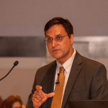 a man wearing a suit and tie speaks into a microphone on stage