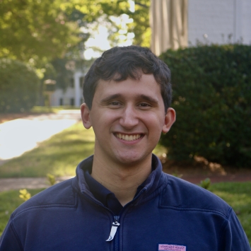 Greg smiling outdoors in a dark blue quarter-zip pullover