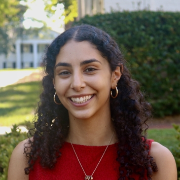 Maya smiling outdoors with curly dark hair and a bright red top