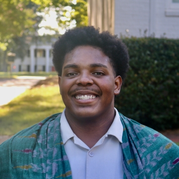 Romeo smiling outdoors in a light dress shirt draped with a patterned teal scarf