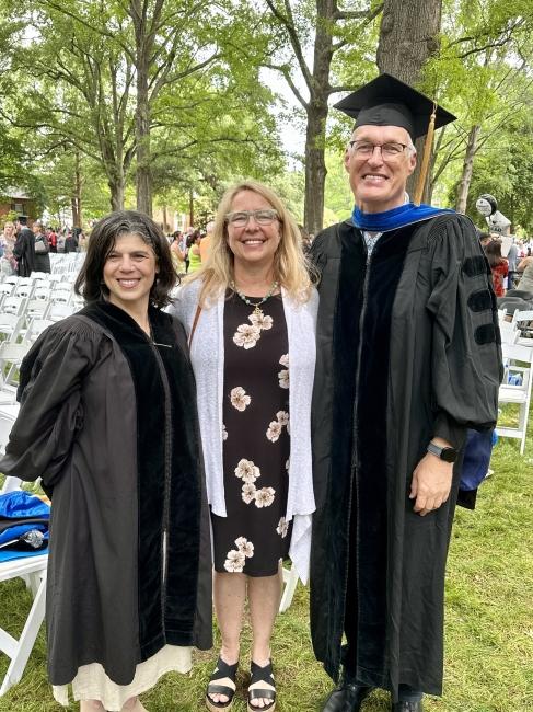 Two professors in commencement regalia with a woman in the middle