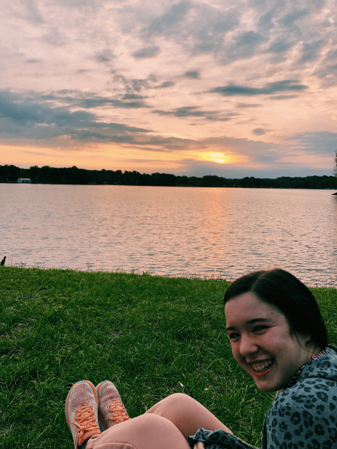 a young woman smiles with a lake and a sunset in the background