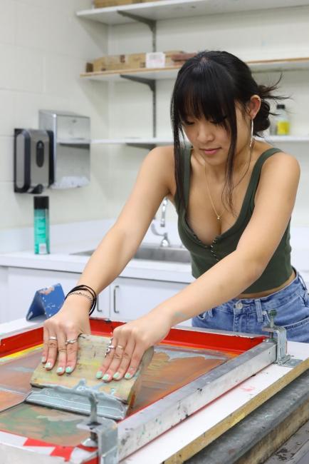 a young woman wears a green tank and jeans while working on a screen printing project in a studio
