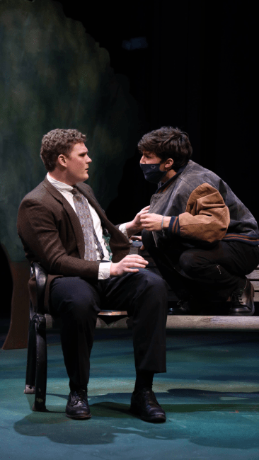two young men sit on a stage while facing each other