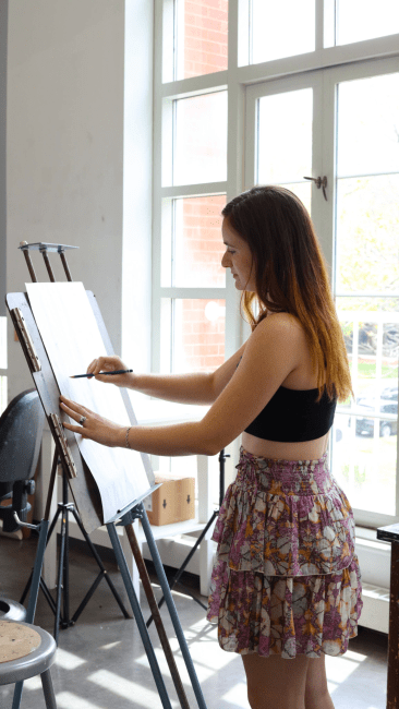 a young woman stands while painting in a bright art studio