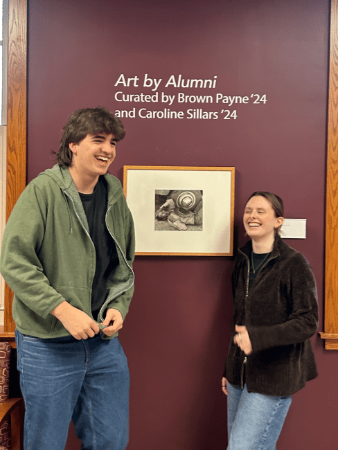 a young man and woman stand next to a piece of art smiling