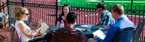Prof. Neumann leads class at an outdoor table with the track and football field in the background