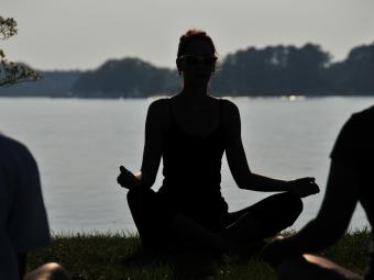 Silhouette of  woman in front of lake doing a yoga pose