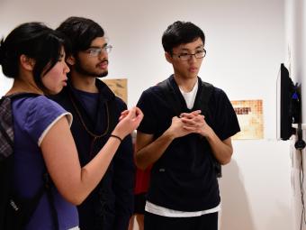 Three students huddle around art work displayed in the gallery and discuss
