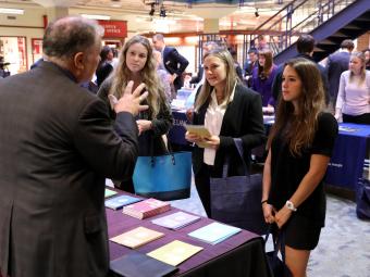 Three students visit a law school fair booth and recruiter talks to them