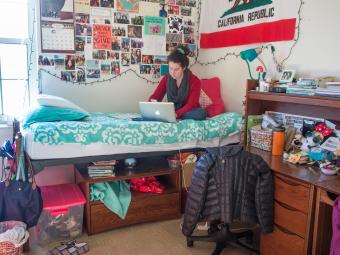 Student sits on her dorm bed and looks at her laptop