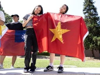 Two young women hold flags of various countries while smiling